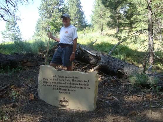 Hiker poses by a rock that has engraved on it "Hello future generations!! Enjoy the Stack Rock trails. The Stack Rock property was acquired with Boise Foothills Levy funds and a generous donation from the Fred Alleman Family. June 2010."