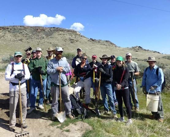 Group posing for photo with shovels, rakes and other tools as they perform trail maintenance.